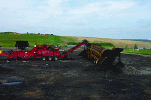 Mark Pahl with Dem-Con Shingle Processing uses a grinder designed specifically to process shingle material. The raw asphalt shingles are first ground to under a 1/2-inch minus size, and that material is then fed to a trommel to reduce the ground shingle material to an even finer size.