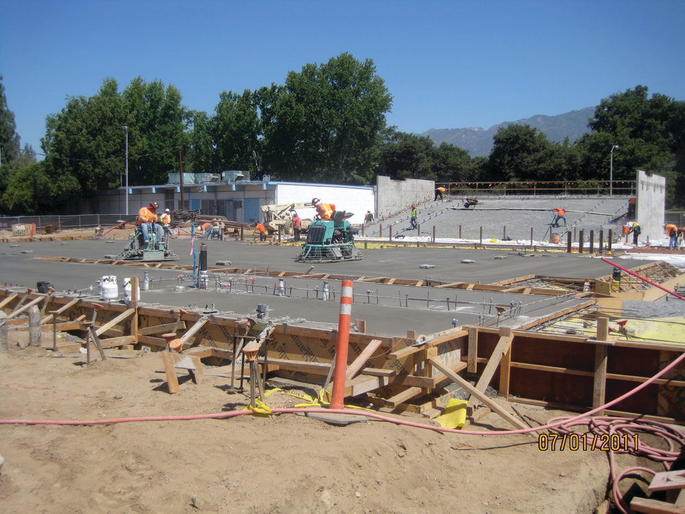 Construction workers pour concrete for the main stage; seating area in the background.