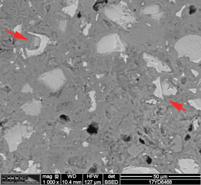 Figure 3. Scanning electron microscope image. Backscatter electron micrograph of polished surface showing detail of cement paste. The image was taken at 1000x magnification. The red arrows show examples of relict and residual cement grains.