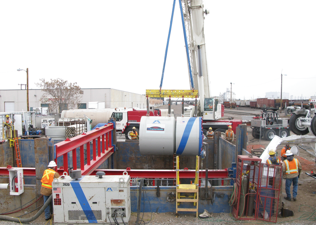 Ground level view of the excavation, showing proximity to an active rail yard, as Microtunnel machine is lowered into the shored excavation.