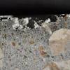 Photograph of polished surface from a concrete core removed from a poorly cured slab on ground showing layer of dark paste at the top of the core. Scale in millimeters. The loss of material at the top is due to poor hydration.