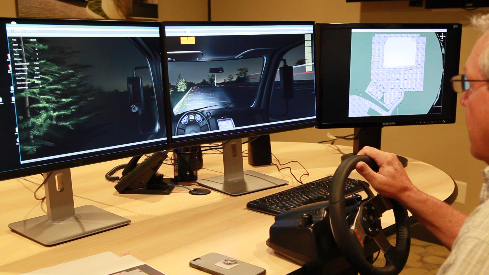 Mike Lucht, 1-800-SWEEPER president and founder, takes a 'test drive' on the organization's new training simulator. Note the trees out the left side view of the cab, the debris field immediately ahead of the sweeper, and the overhead view on the right-hand screen.
