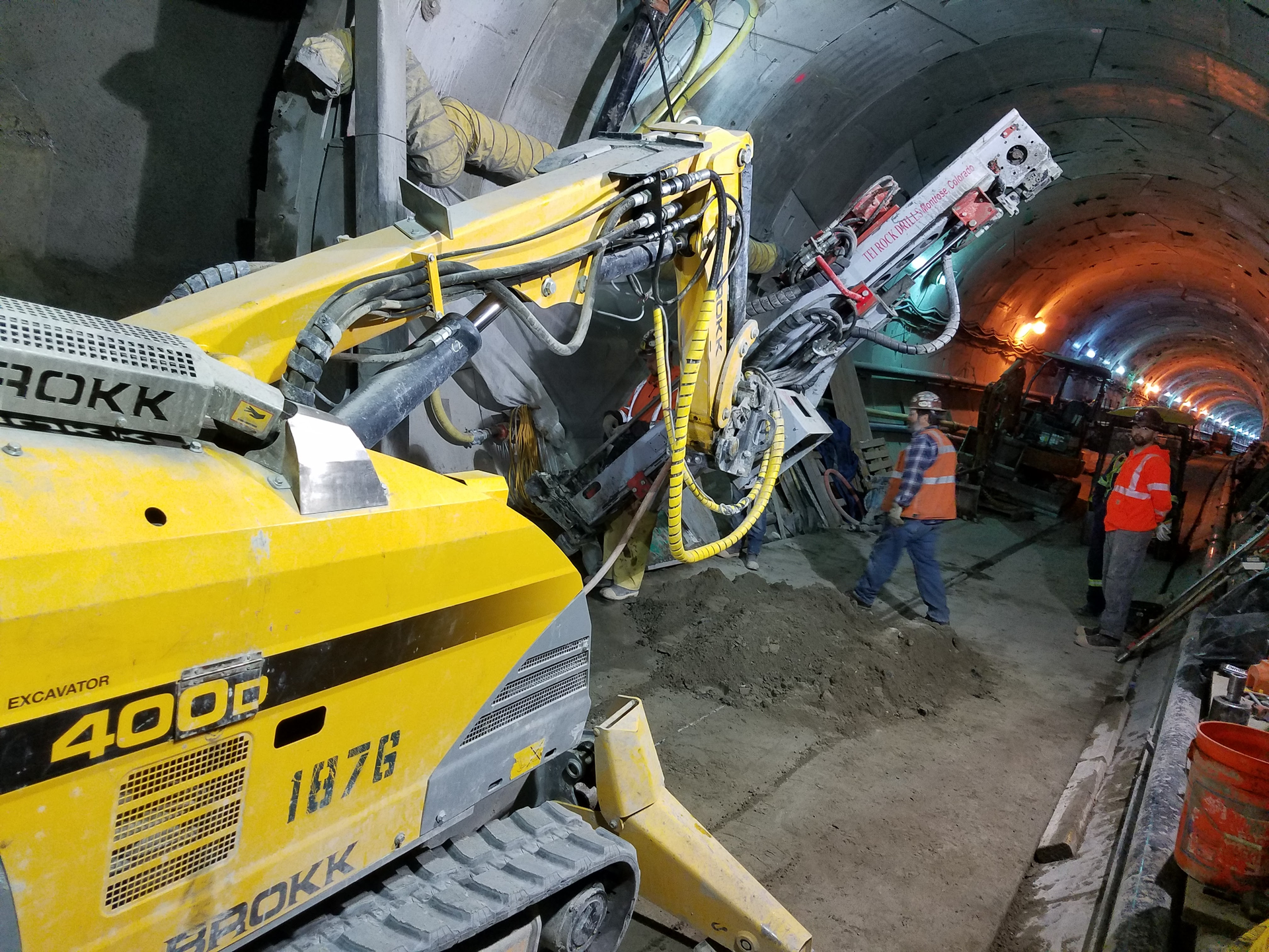 Workers use a Brokk 400D with a TEI 350 rock drill to drill through a tunnel wall. Crews used the attachment to drill holes for steel spiles, well points and freeze pipes.