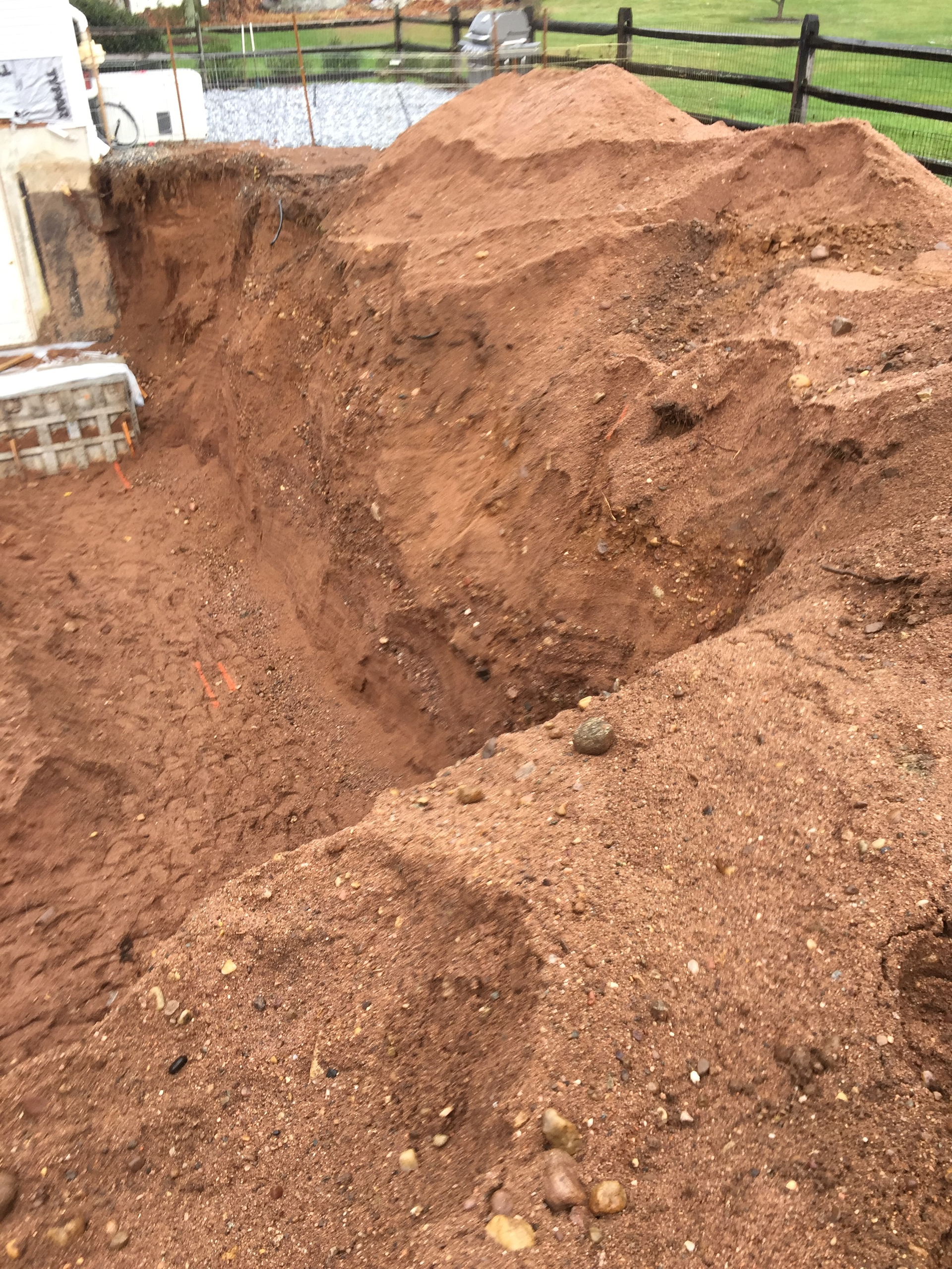 Figure 1: Residential basement excavation with over 8-ft of depth. No benching, loose soil encumbrances on the slope and spoil piles closer than 2-ft from the opening. This excavation should not be entered until corrected.