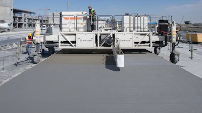 The integrated spraying system of the Wirtgen TCM 95 texture curing machine is spreading a dispersion on the concrete surface. It prevents premature drying of the concrete surface and edges.