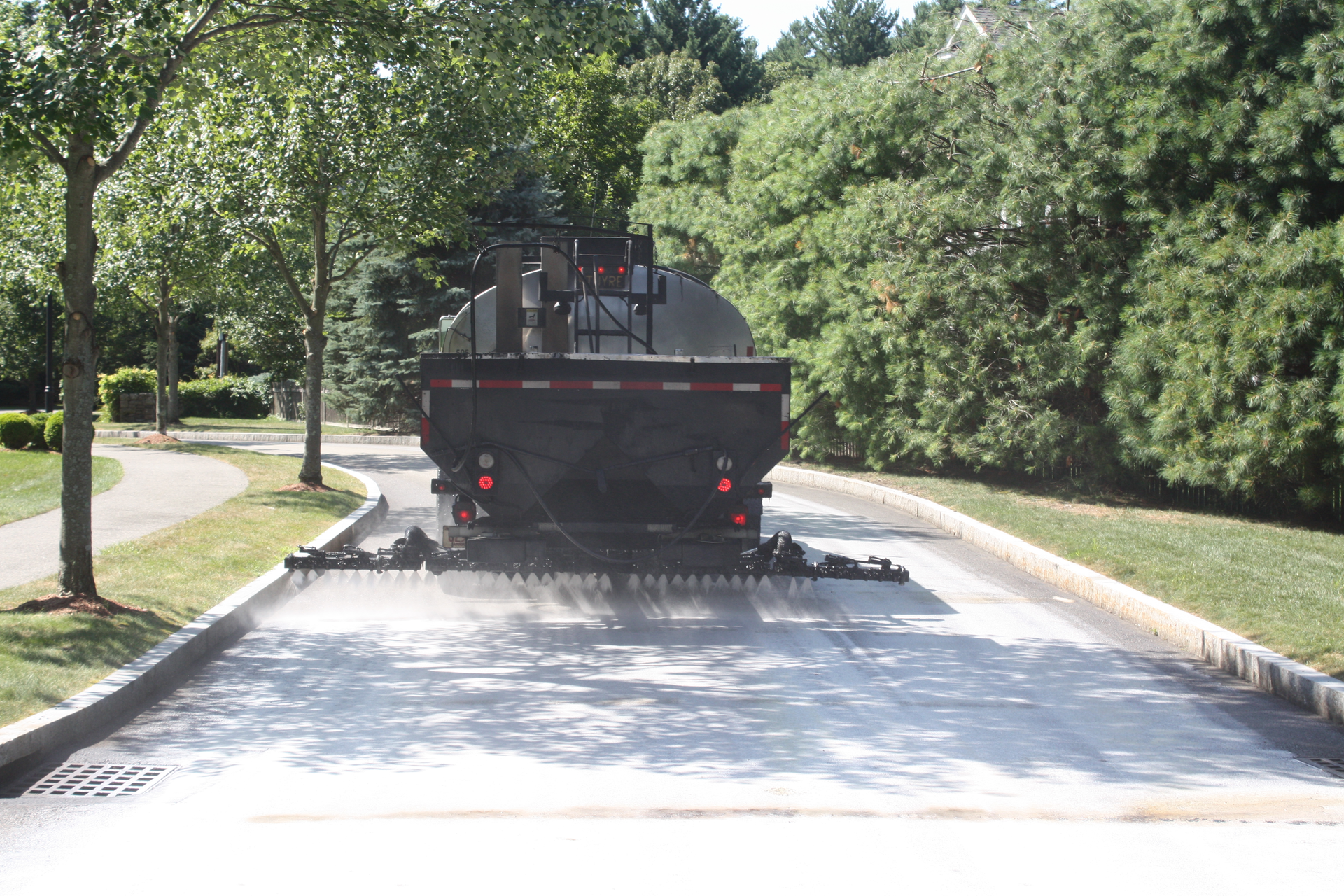 Contractor Indus employs a 2000-gallon Etnyre distributor to spray Delta Mist penetrating asphalt rejuvenator on a local street in historic Lexington, MA.