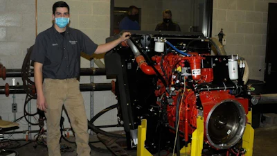 Michael J. Sormilic, an online power generation student from Southbury, Conn., who has spent much of the Fall 2020 semester learning the ins and outs of the equipment, stands alongside a Cummins crane engine donated to Pennsylvania College of Technology by Terex Corp. Behind him, in the control room of the dyno lab, are John D. Motto (left), diesel equipment technology instructor, and Chris Macdonald, assistant director of corporate relations.