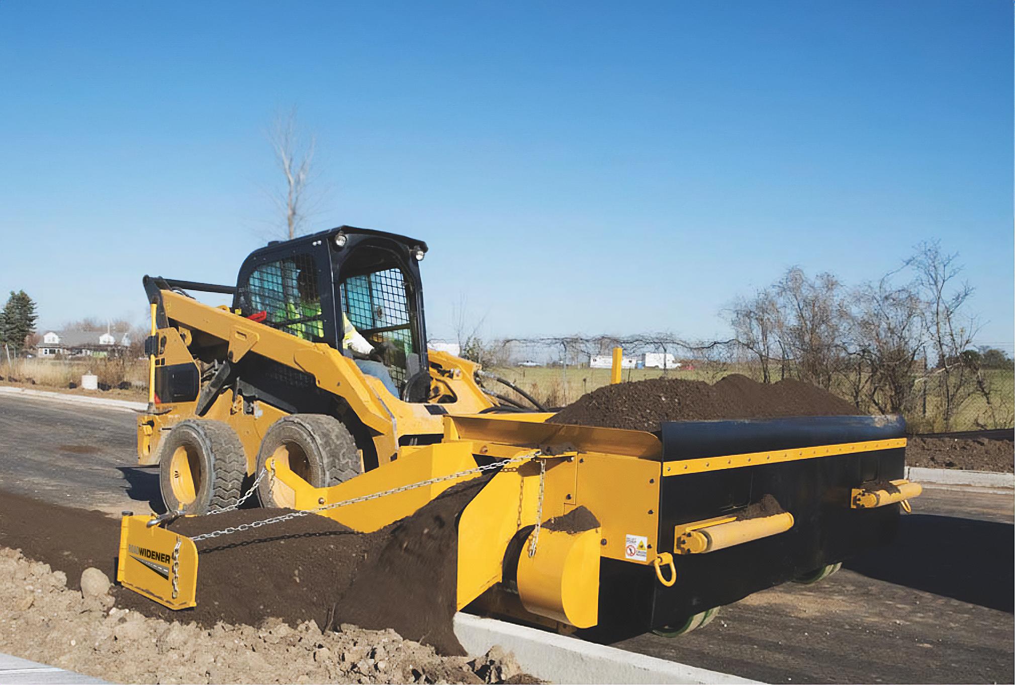 The accessory extends to the left or right of the FH-R and dispenses material over the curb to backfill with dirt or aggregate.