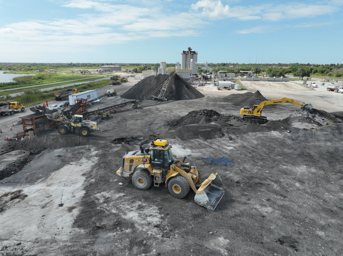 Teleo-equipped Caterpillar wheel loader operating in the midst of other operations across an Ajax Paving asphalt plant.