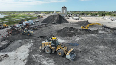 Teleo-equipped Caterpillar wheel loader operating in the midst of other operations across an Ajax Paving asphalt plant.
