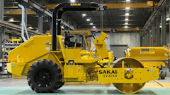Yellow Sakai industrial road roller in manufacturing facility with overhead crane