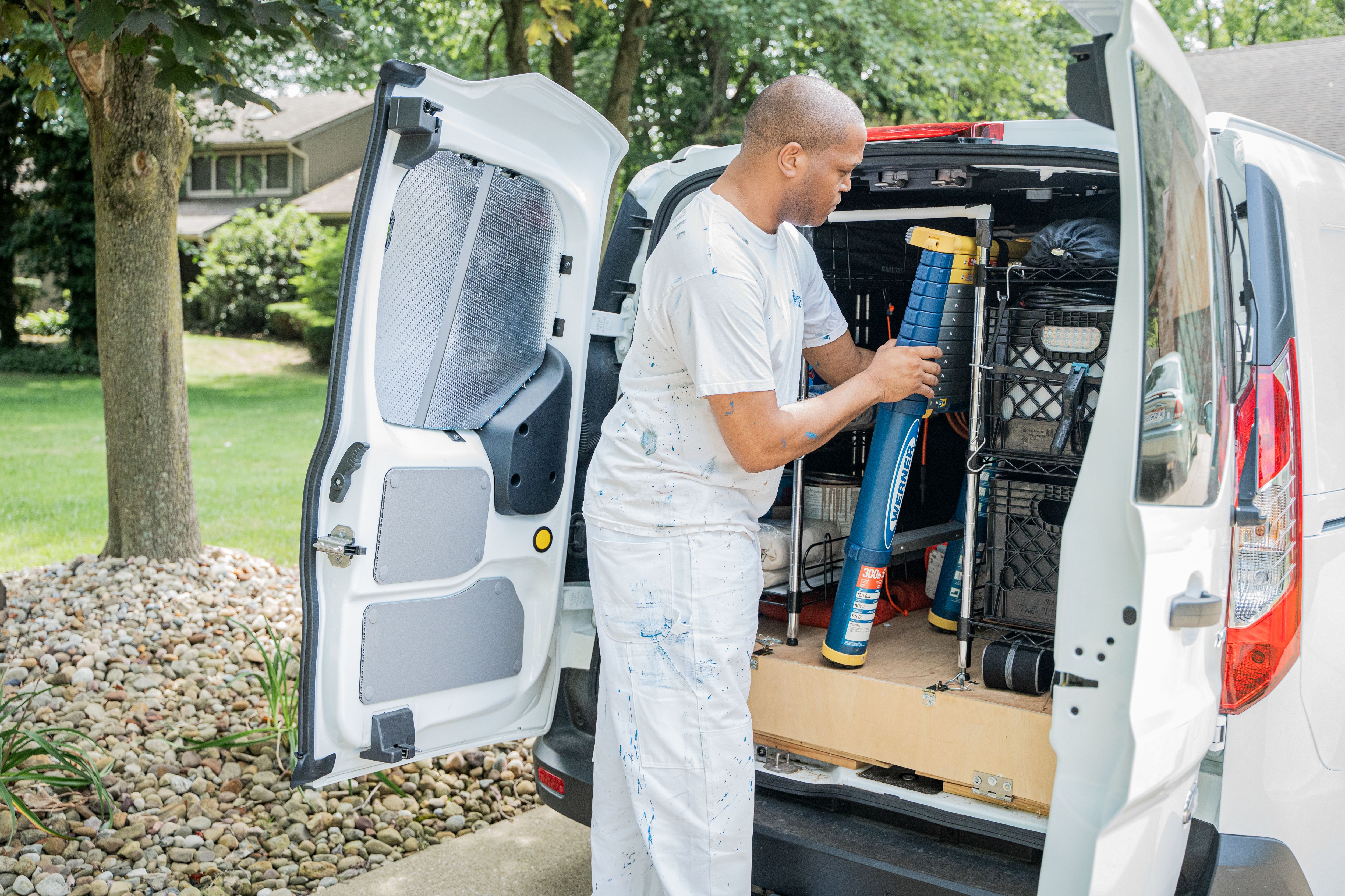 Painter organizing tools in white van parked on residential street