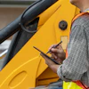 Worker in safety vest using tablet near yellow construction equipment