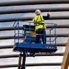 Construction worker on elevated blue lift platform performing maintenance work