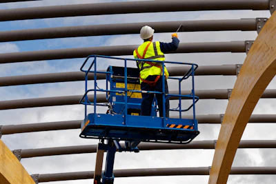 Construction worker on elevated blue lift platform performing maintenance work