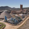 Industrial processing facility with blue tanks and machinery in mountainous forest landscape