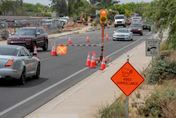 Road construction zone with safety cones, traffic signal, and vehicles navigating restricted lane