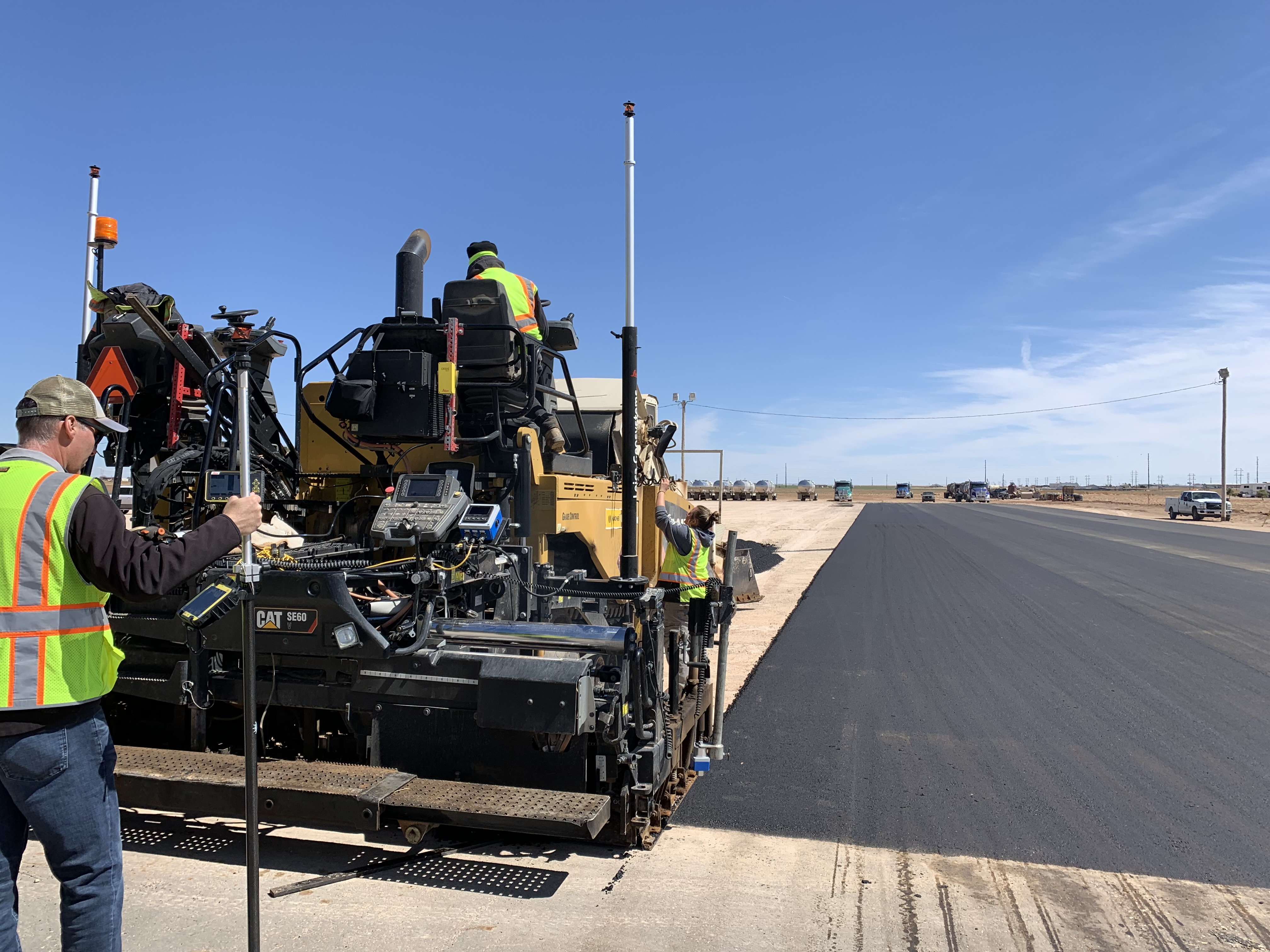 Road construction crew operating asphalt paver on desert highway