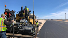 Road construction crew operating asphalt paver on desert highway