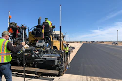 Road construction crew operating asphalt paver on desert highway