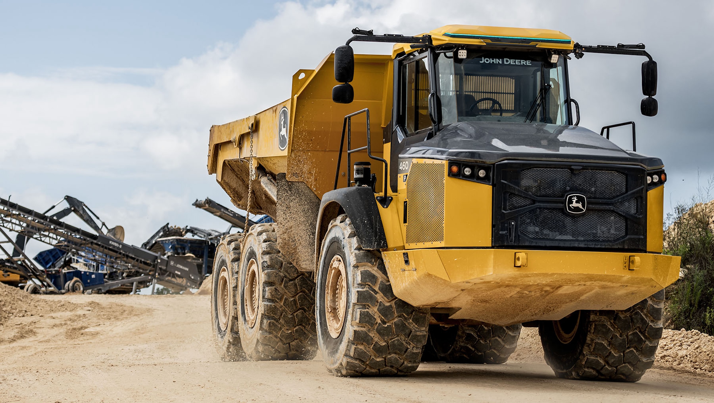 Yellow John Deere articulated dump truck on dusty construction site with industrial equipment