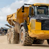 Yellow John Deere articulated dump truck on dusty construction site with industrial equipment