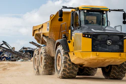 Yellow John Deere articulated dump truck on dusty construction site with industrial equipment