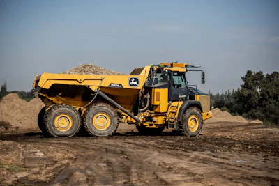Yellow John Deere articulated dump truck hauling gravel at construction site