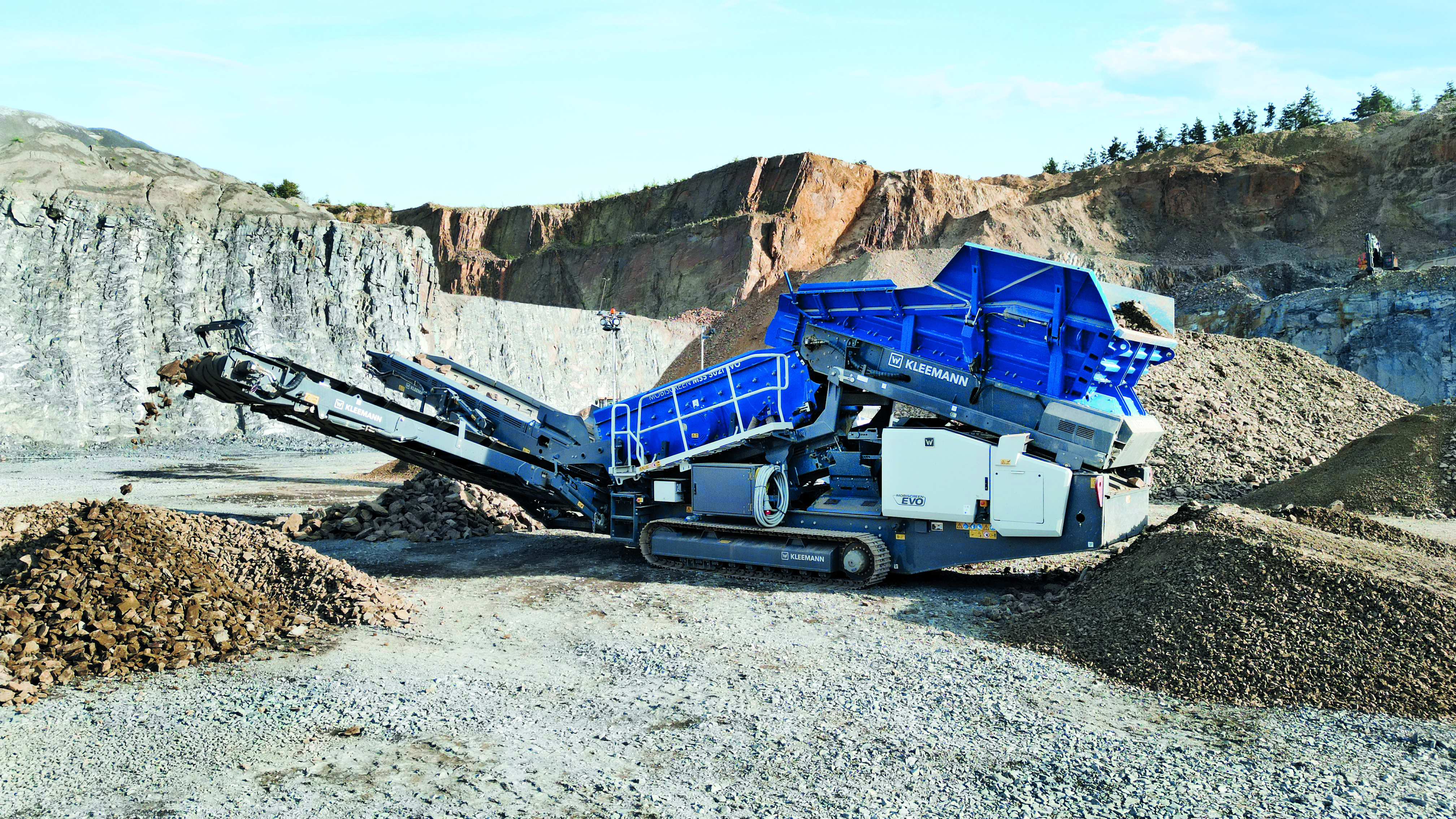 Industrial mobile rock crusher in quarry with stone piles and rocky landscape