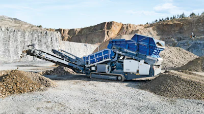 Industrial mobile rock crusher in quarry with stone piles and rocky landscape
