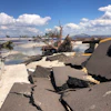 Destroyed coastal highway with cracked pavement and storm debris near bridge