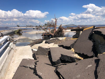 Destroyed coastal highway with cracked pavement and storm debris near bridge