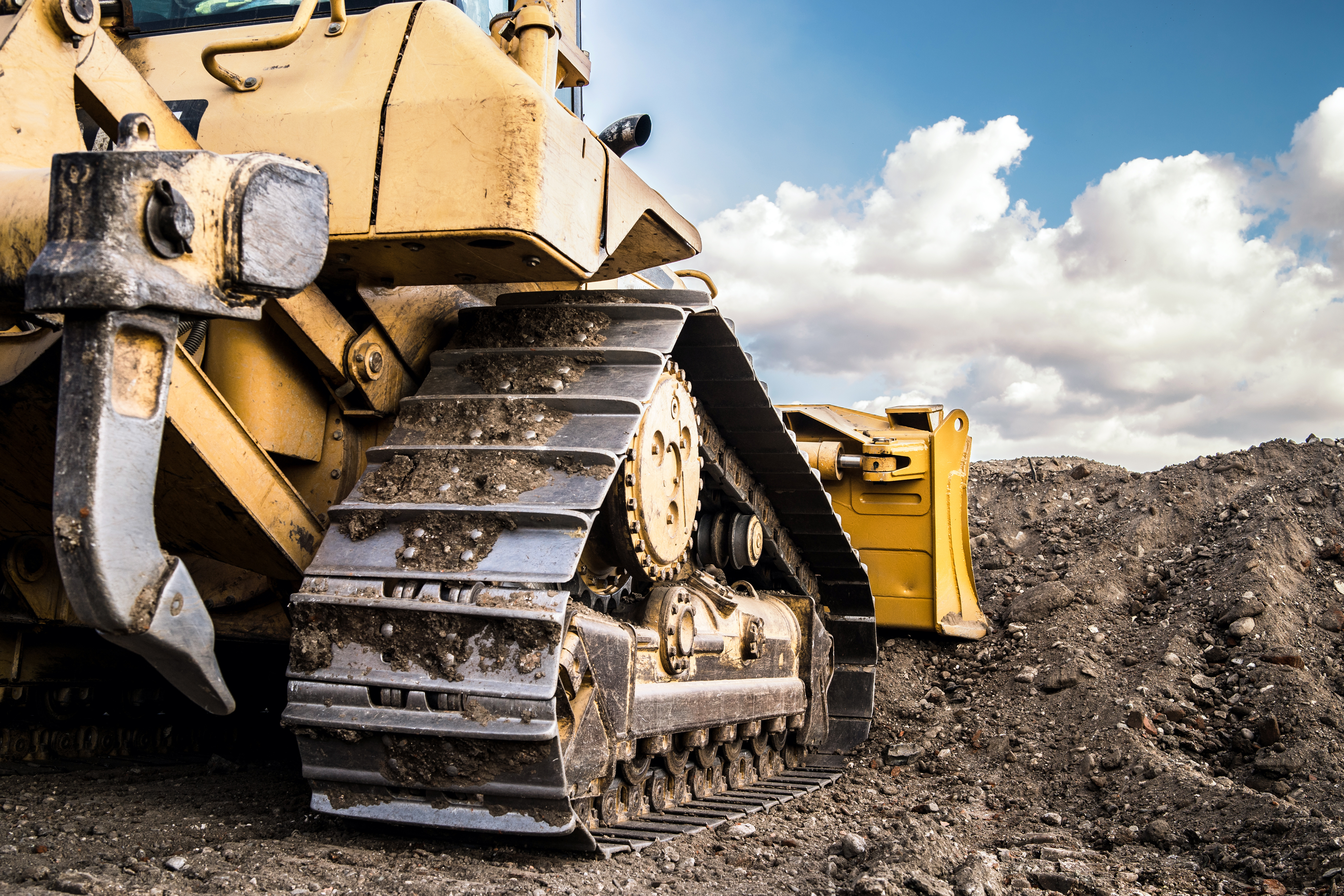 Yellow bulldozer on rocky ground with heavy-duty tracks and cloudy sky