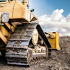 Yellow bulldozer on rocky ground with heavy-duty tracks and cloudy sky