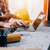 Construction professional reviewing architectural blueprints on laptop with safety helmet