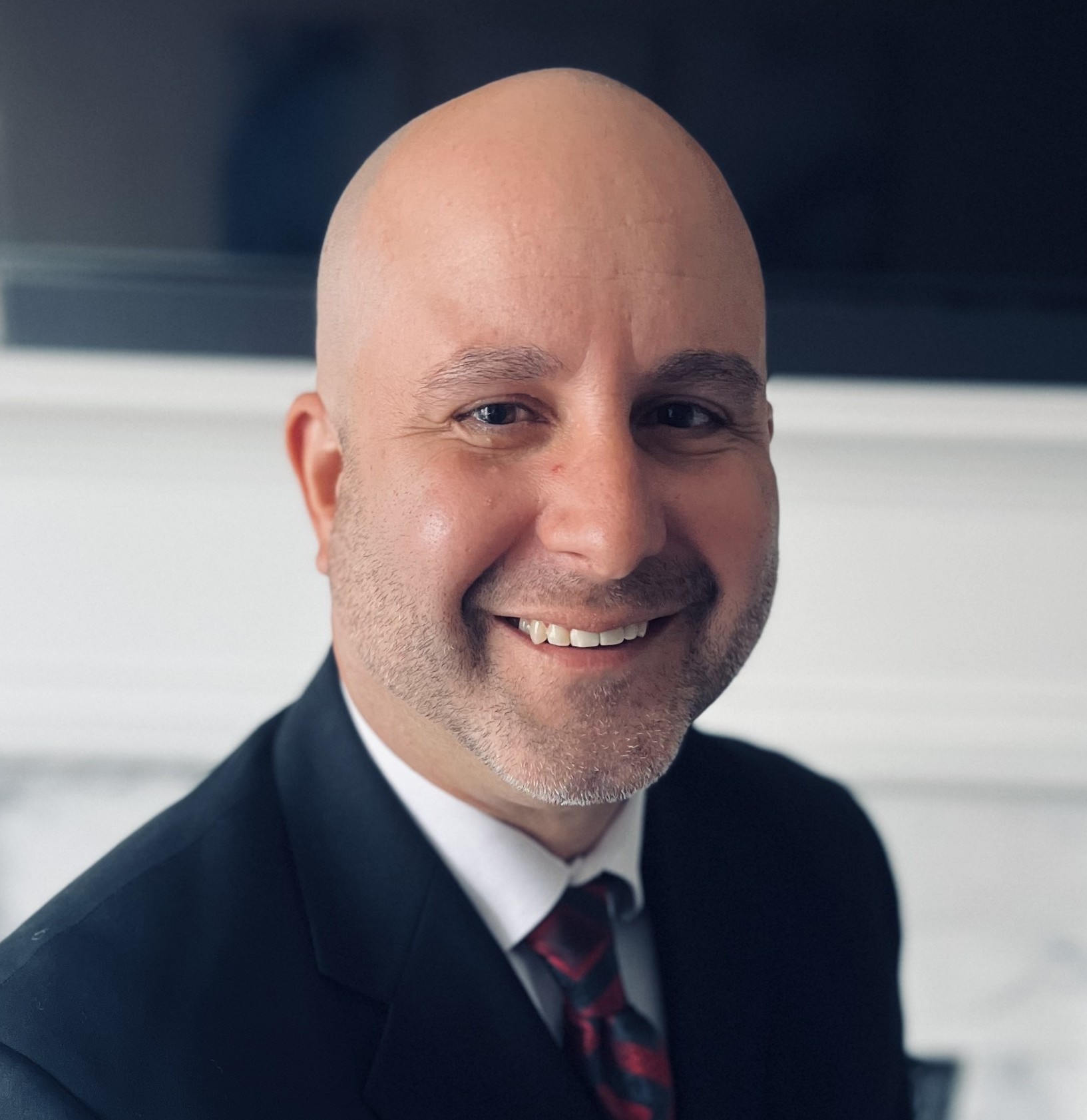 Smiling professional in navy suit and striped tie, bald with beard