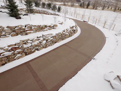 Curved winter walkway with stone wall amid snowy landscape and evergreen trees