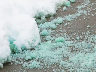 Mint green and white crystalline salt or snow scattered on a gray surface