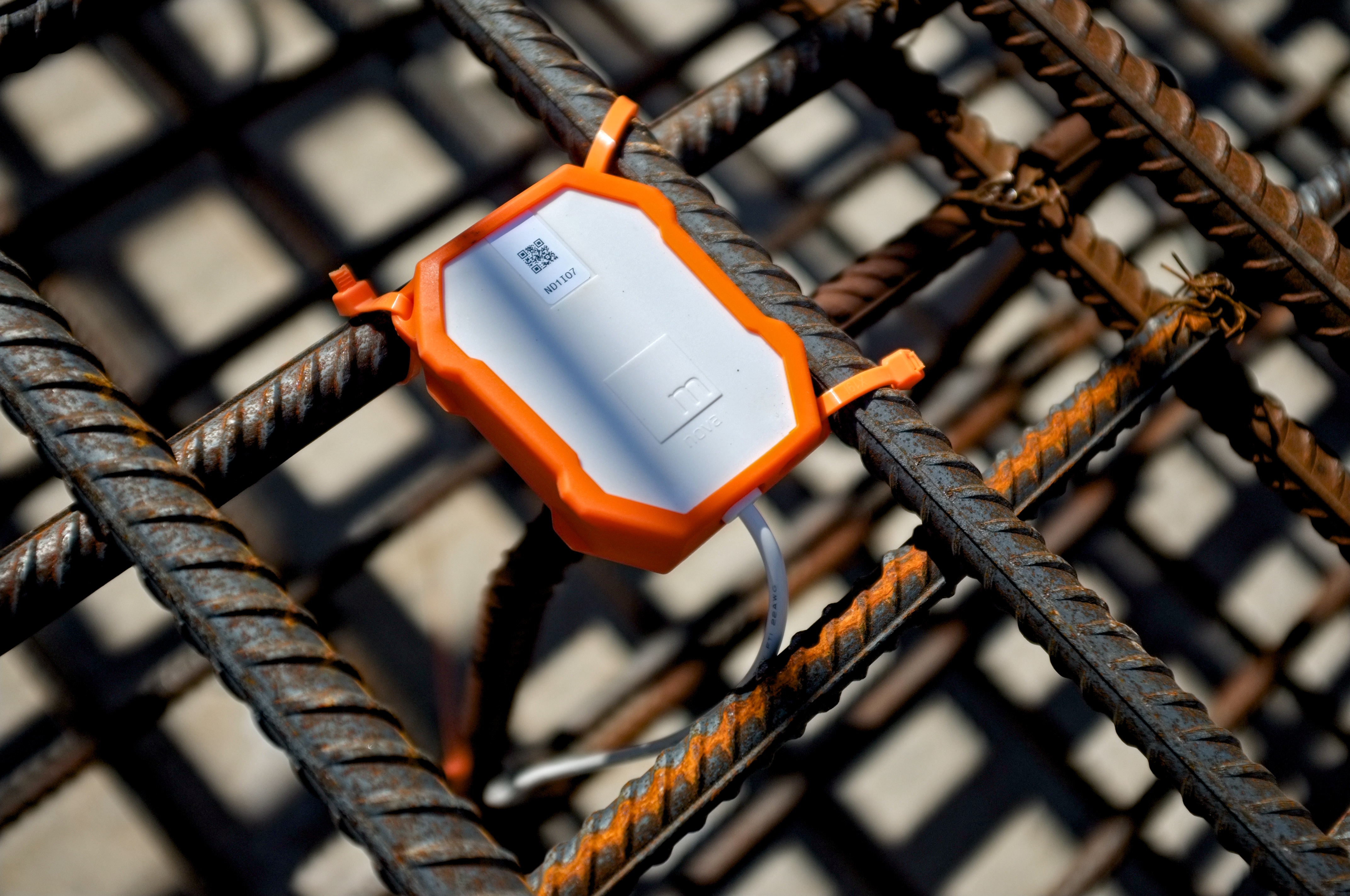 Orange protective sensor mounted on steel rebar with white document inside