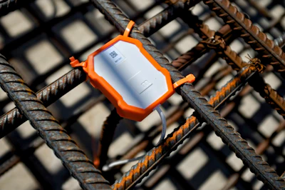 Orange protective sensor mounted on steel rebar with white document inside