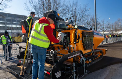 Construction workers operating a yellow asphalt paver on a road project
