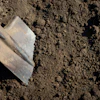 Worn metal garden shovel resting on dark, textured soil