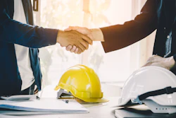 Business professionals shaking hands near yellow and white construction helmets