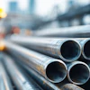 Steel industrial pipes stacked at construction site with worker in background