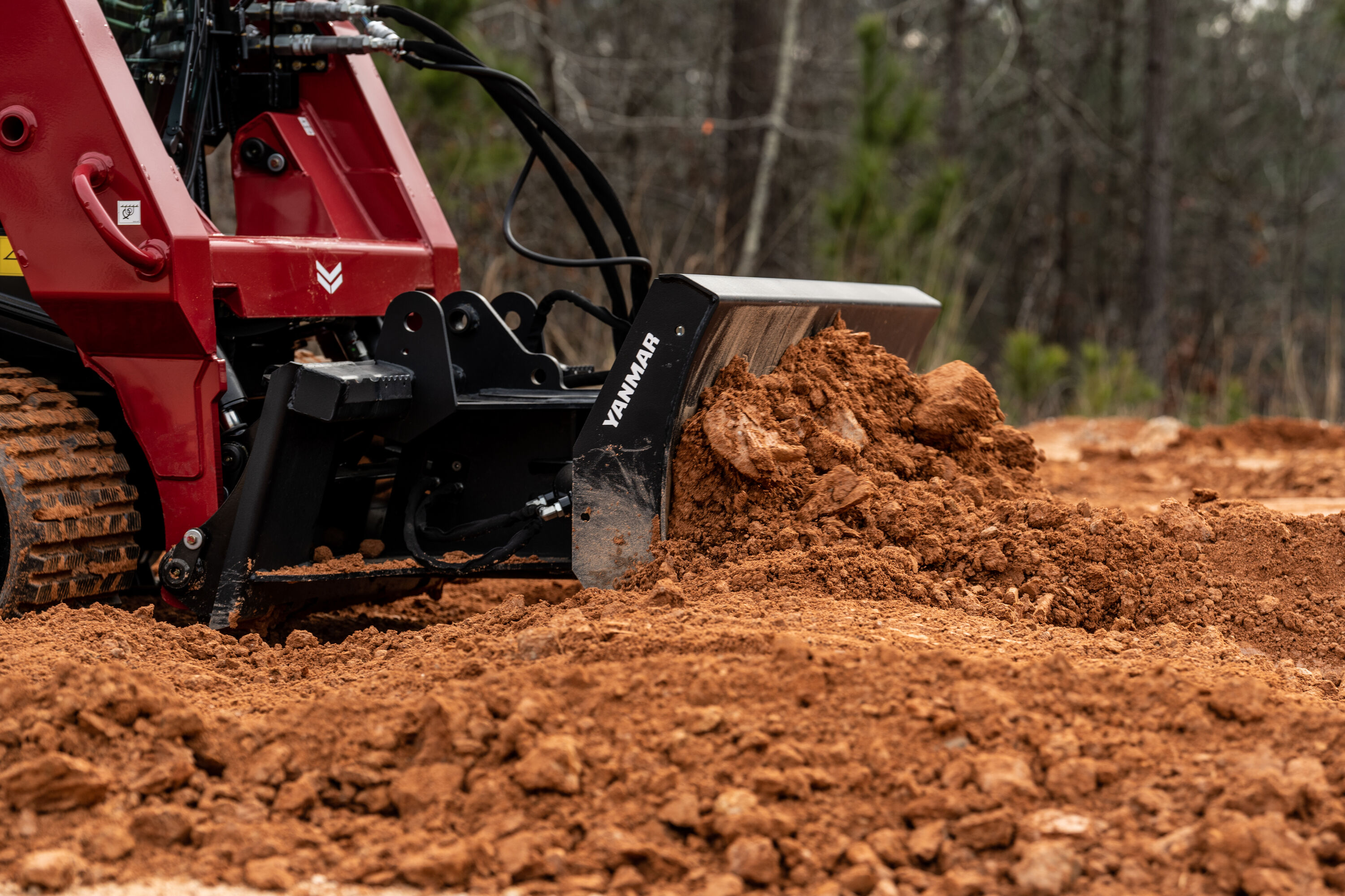Yanmar construction machine moving red soil in wooded terrain