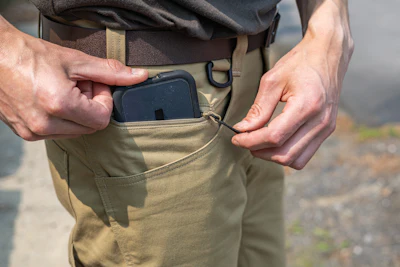 Hands placing a black device into a khaki pants pocket
