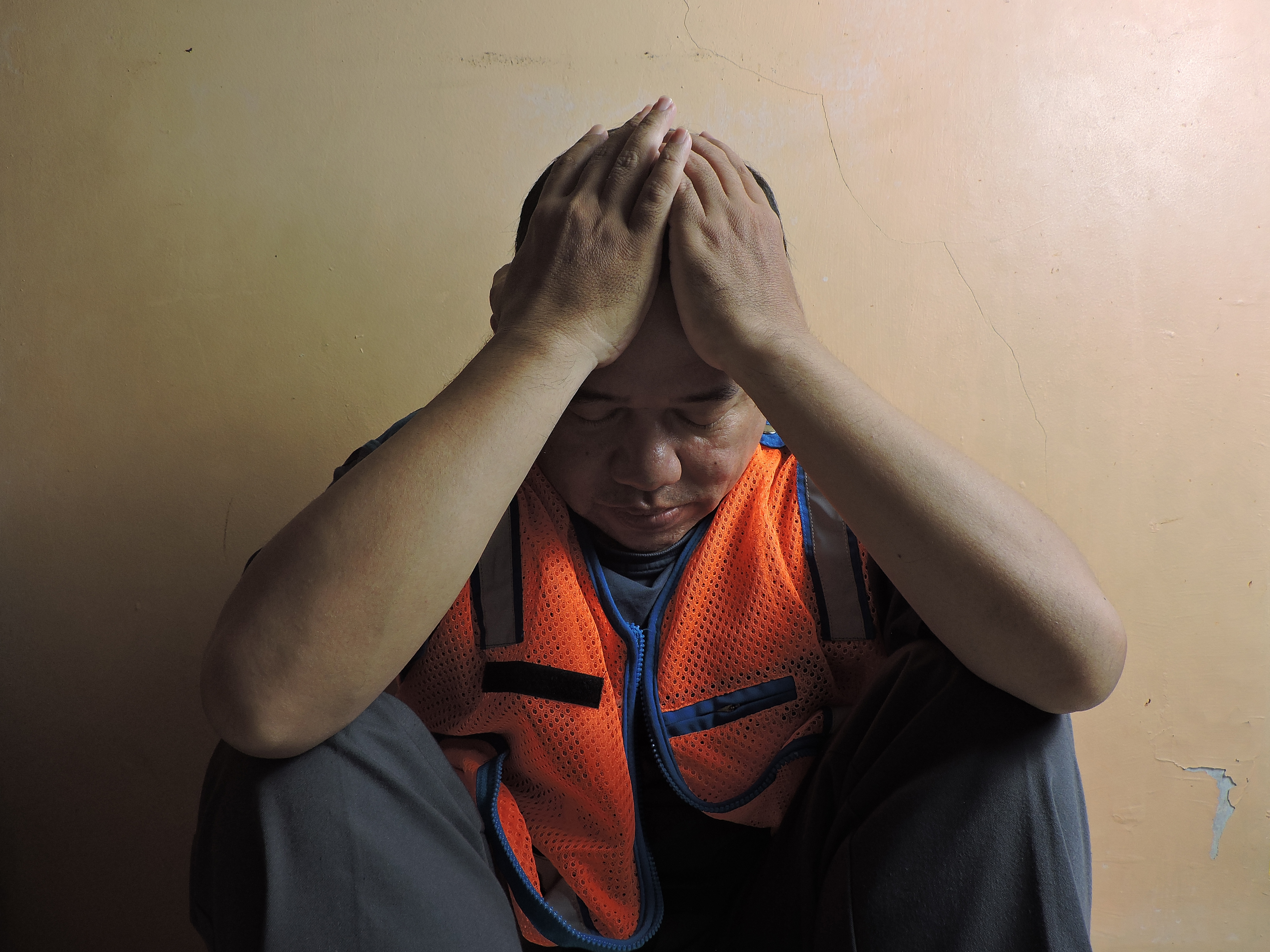 Worker in orange safety vest covering face, showing emotional exhaustion