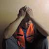 Worker in orange safety vest covering face, showing emotional exhaustion