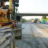 Yellow motor grader on road construction site with highway overpass