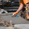 Construction workers pouring and smoothing concrete sidewalk with safety cone
